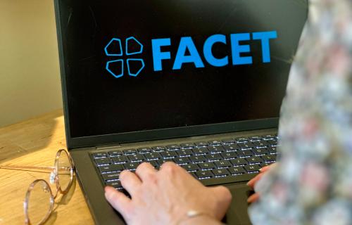 A laptop with the FACET logo on a desk.