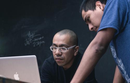 Two people working on a laptop in a classroom.