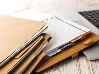 Folders and a planner on a wooden desk next to a laptop.